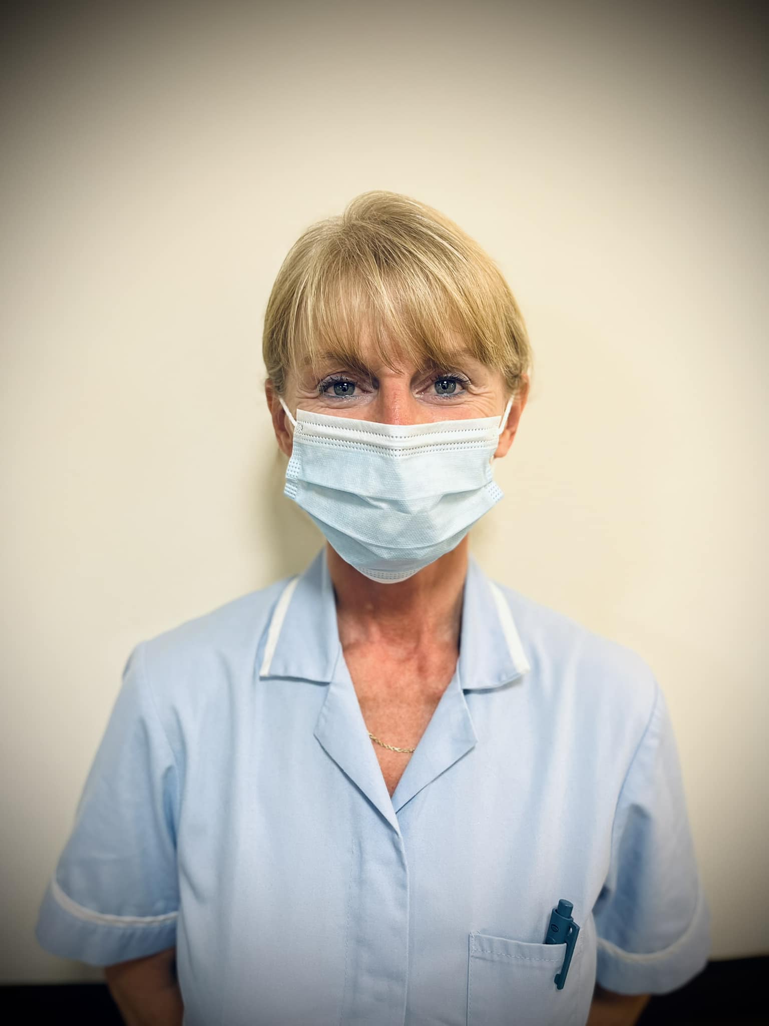 A female carer with a face mask on in a light blue uniform.