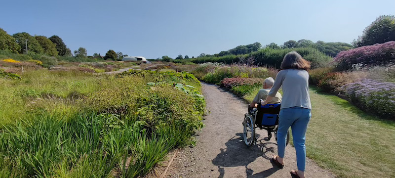 resident in wheelchair being taken through a local garden by one of our team