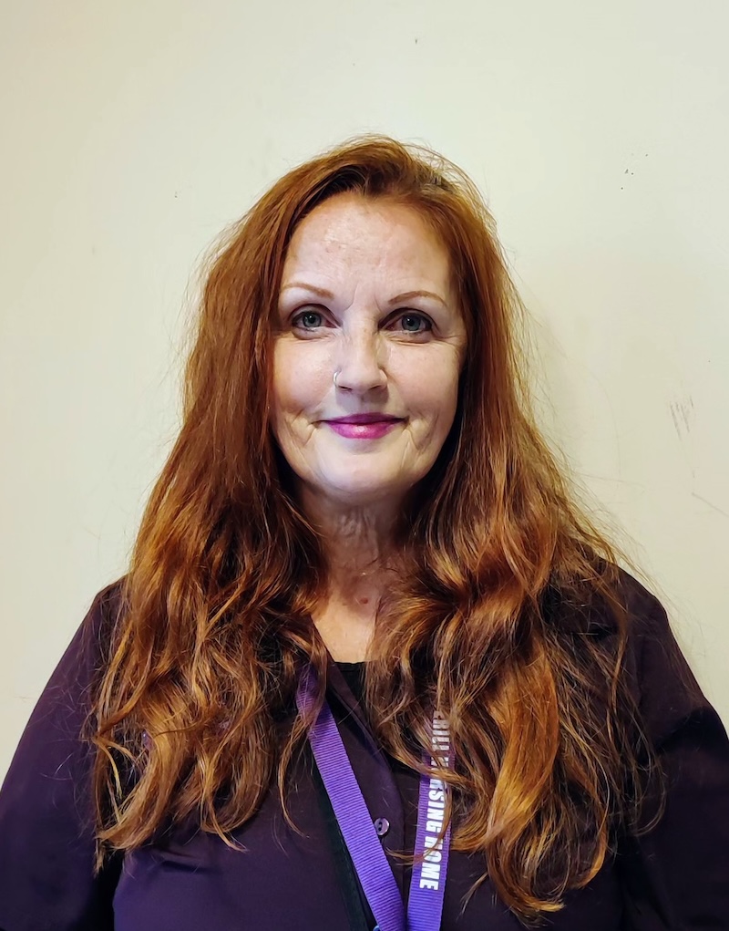 Female with ginger hair wearing a black uniform and purple lanyard for a team headshot