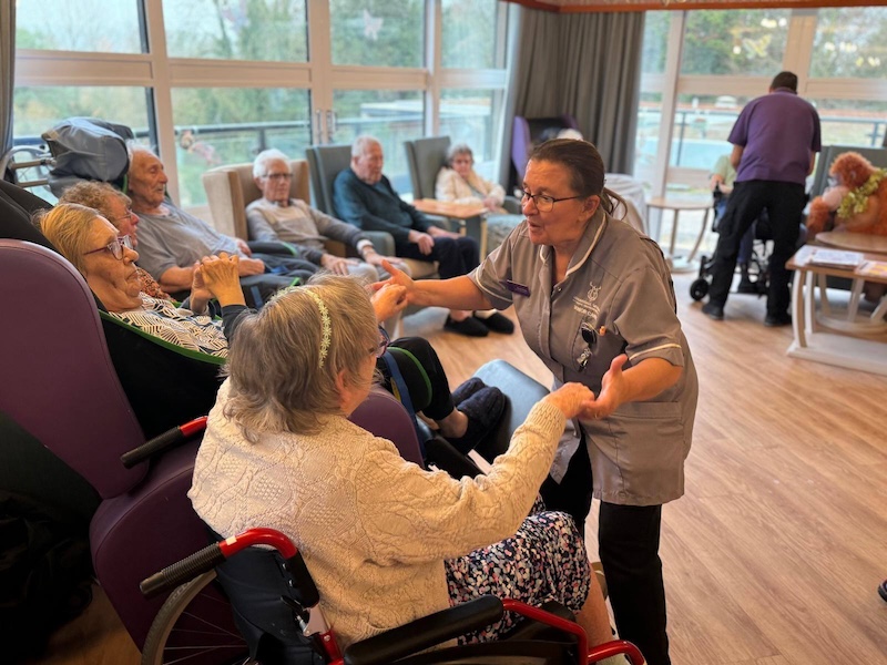 female carer holding hands with a resident and dancing in the lounge