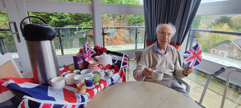 male resident sat with a cup of tea and union jack flag in his hands smiling