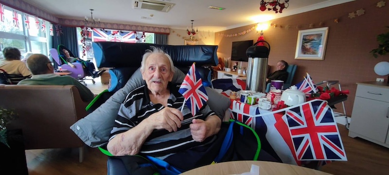 male resident sat in an armchair smiling holding union jacks on remembrance day