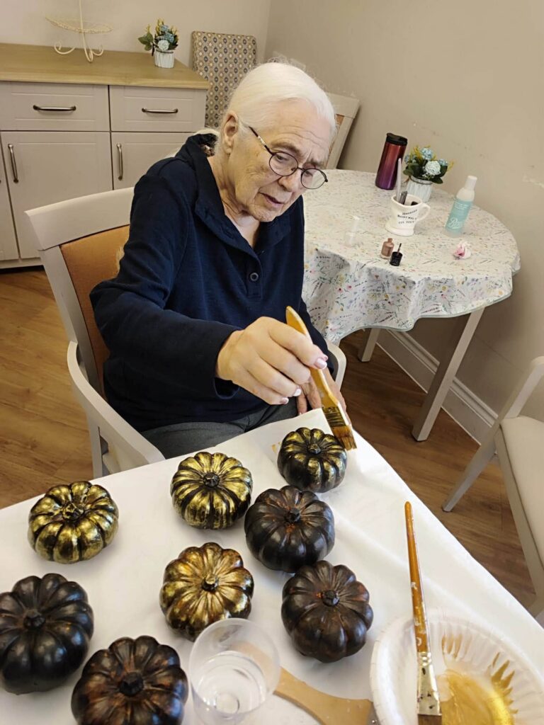 an older lady painting pumpkin ornaments