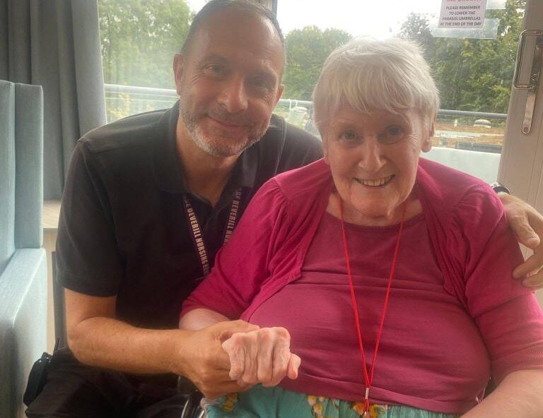 older lady sat in a wheelchair with a man holding her hand