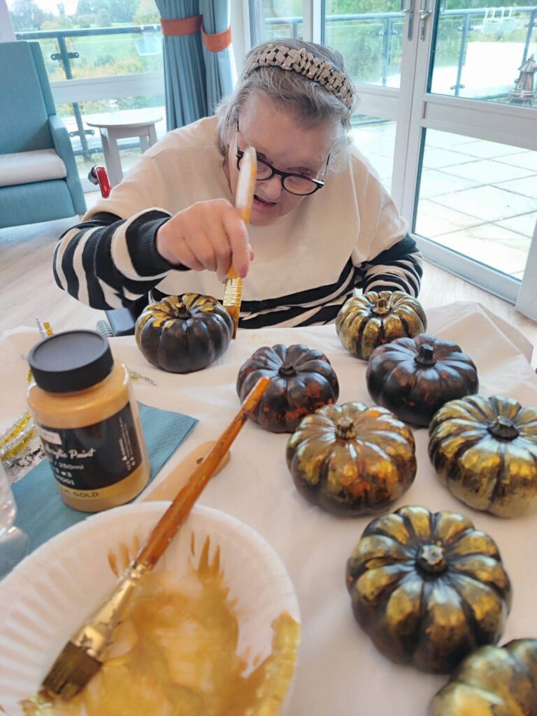 an older lady painting pumpkin ornaments
